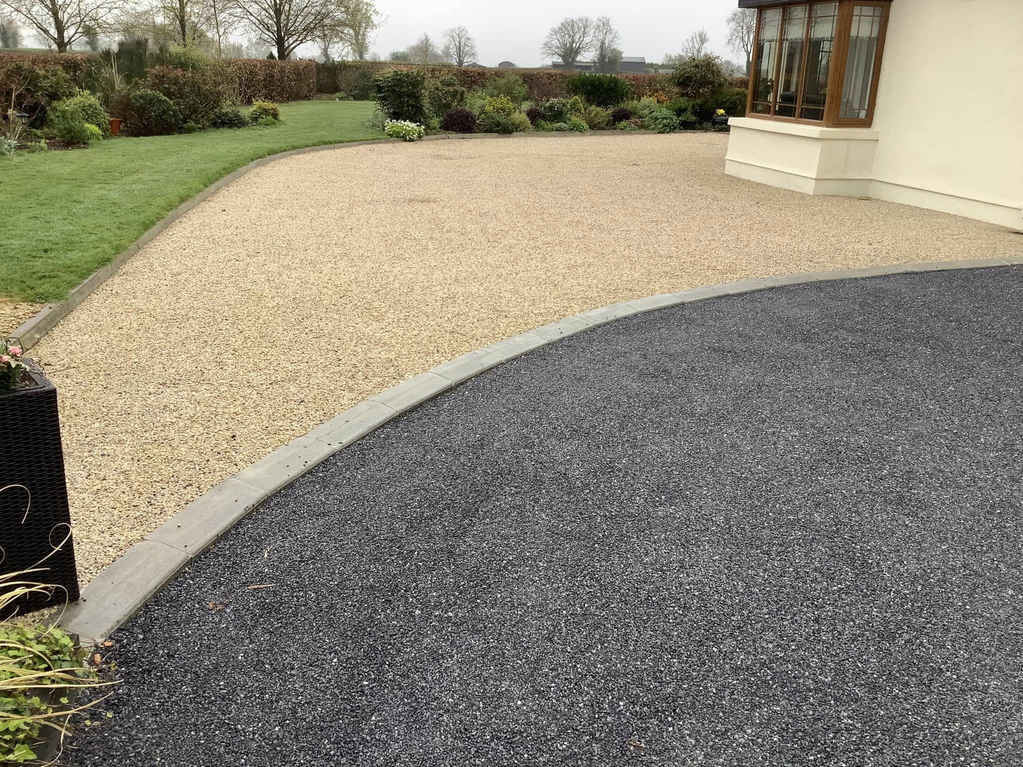 side of a house and a driveway divided by stone edging with different coloured chip on either side