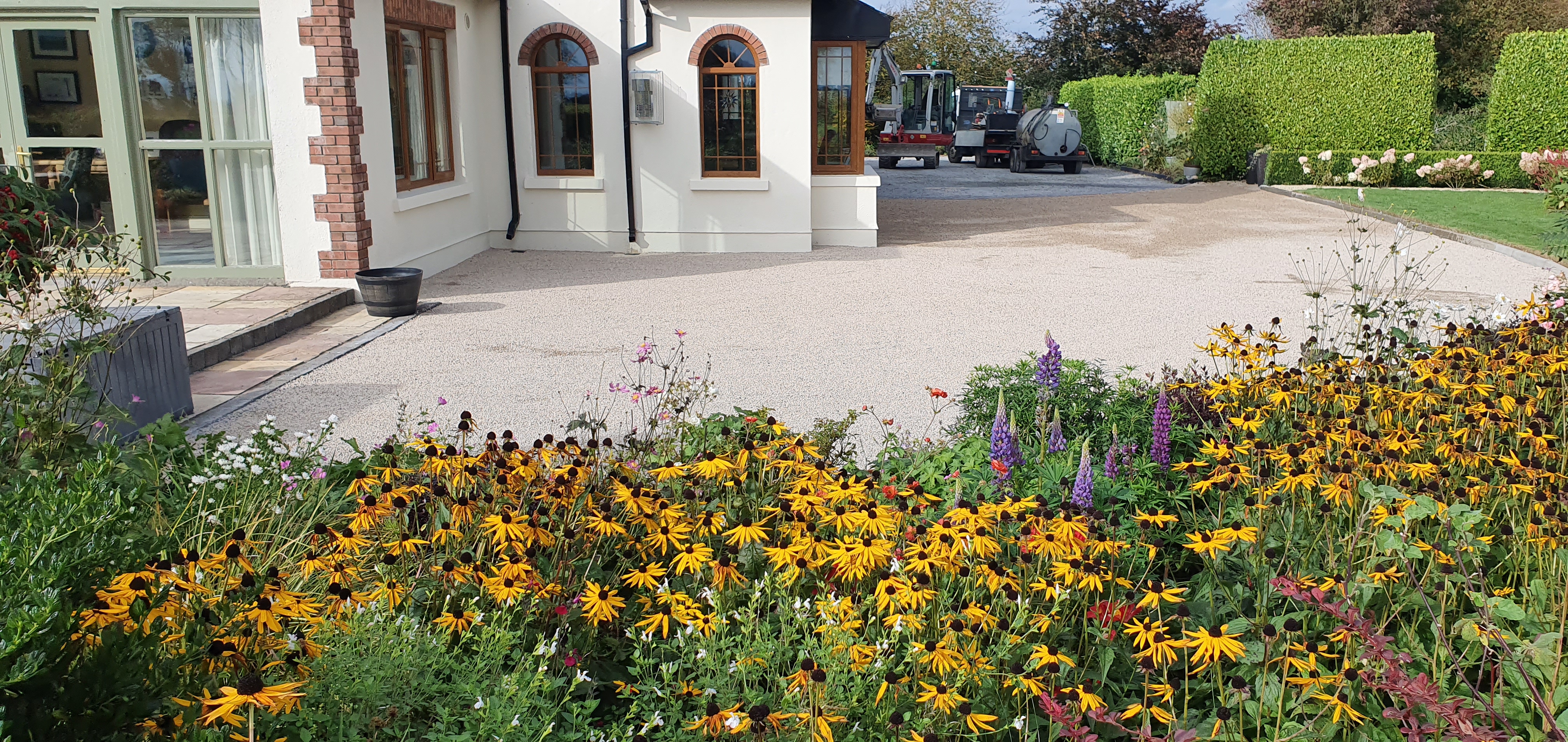 Tar and chip driveway in front of patio door surrounded by flowers.