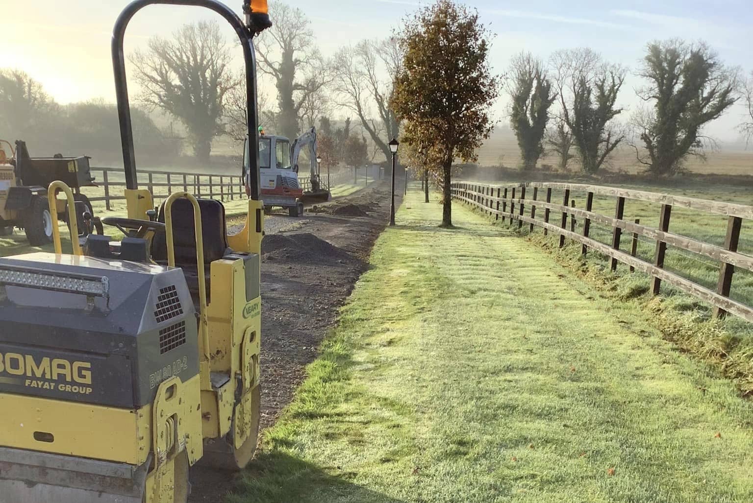 A digger and a roller preparing a driveway for a tar and chip paving